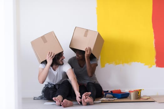 Happy young multiethnic couple relaxing and playing with cardboard boxes after painting a room in their new house on the floor