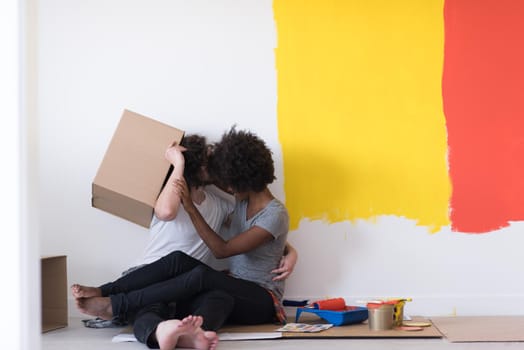 Happy young multiethnic couple relaxing and playing with cardboard boxes after painting a room in their new house on the floor