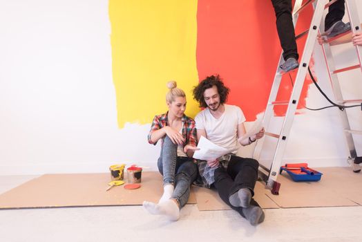 Happy young couple relaxing after painting a room in their new house on the floor