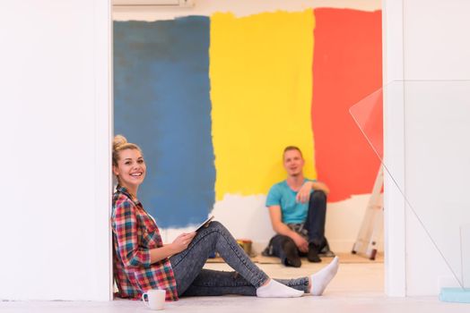 Happy young couple relaxing after painting a room in their new house on the floor