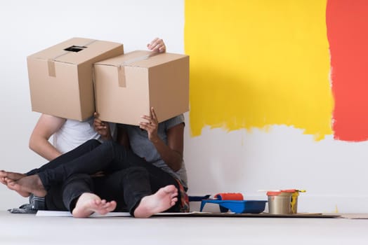 Happy young multiethnic couple relaxing and playing with cardboard boxes after painting a room in their new house on the floor