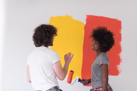 happy young multiethnic couple painting interior wall of new house