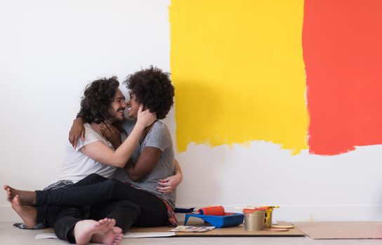 Happy young multiethnic couple relaxing after painting a room in their new house on the floor