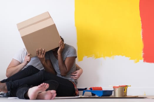 Happy young multiethnic couple relaxing and playing with cardboard boxes after painting a room in their new house on the floor