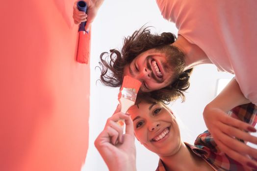 happy smiling young couple painting interior wall of new house