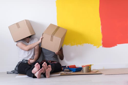 Happy young multiethnic couple relaxing and playing with cardboard boxes after painting a room in their new house on the floor