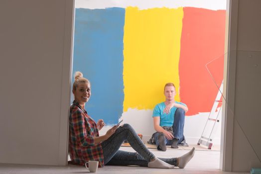 Happy young couple relaxing after painting a room in their new house on the floor