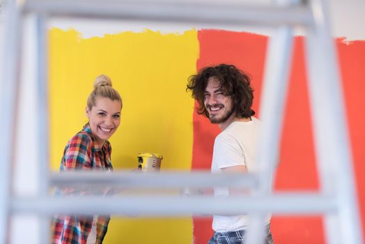 happy smiling young couple painting interior wall of new house