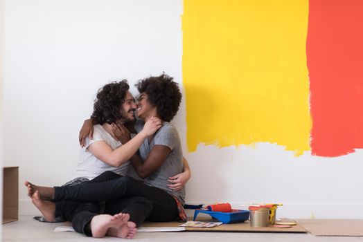 Happy young multiethnic couple relaxing after painting a room in their new house on the floor