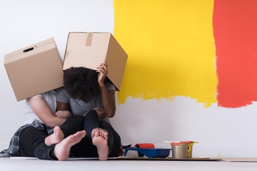 Happy young multiethnic couple relaxing and playing with cardboard boxes after painting a room in their new house on the floor