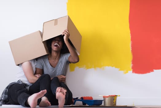 Happy young multiethnic couple relaxing and playing with cardboard boxes after painting a room in their new house on the floor