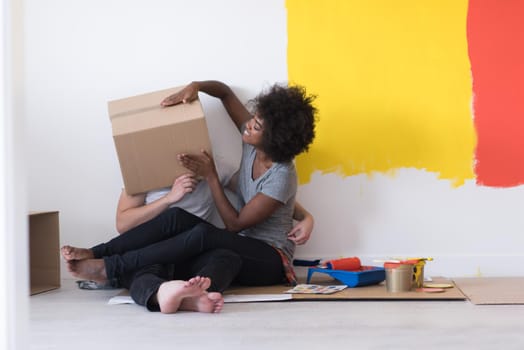 Happy young multiethnic couple relaxing and playing with cardboard boxes after painting a room in their new house on the floor