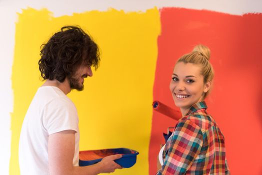 happy smiling young couple painting interior wall of new house