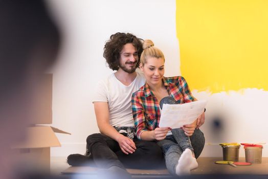 Happy young couple relaxing after painting a room in their new house on the floor