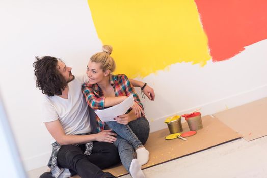 Happy young couple relaxing after painting a room in their new house on the floor