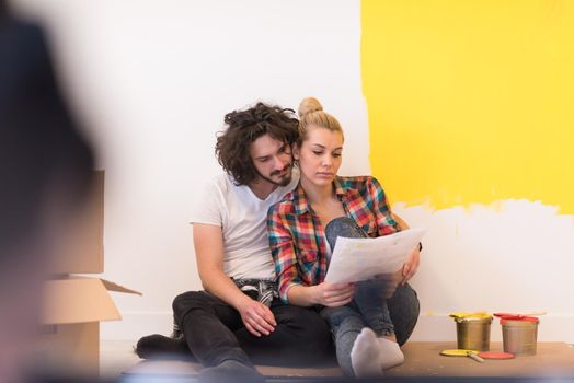 Happy young couple relaxing after painting a room in their new house on the floor