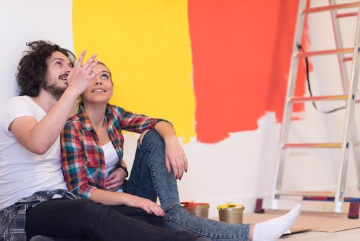 Happy young couple relaxing after painting a room in their new house on the floor