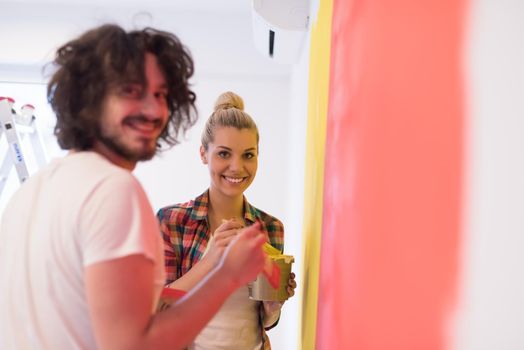 happy smiling young couple painting interior wall of new house