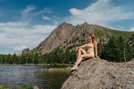 Tourist girl enjoys the magical view of the lake, coniferous forest and magical view sitting on big stone on the shore of a turquoise lake in the mountains. Hiking in the Natural Park. Black lake.