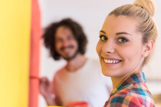 happy smiling young couple painting interior wall of new house