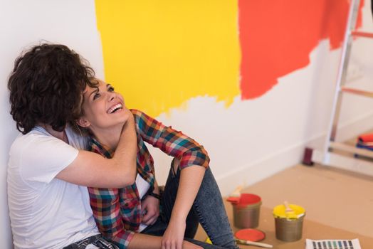 Happy young couple relaxing after painting a room in their new house on the floor
