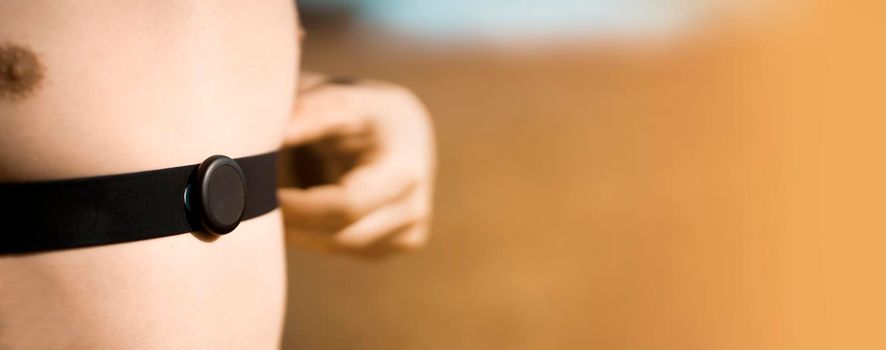 A young male athlete puts on a heart rate monitor and smart watch before jogging in nature. A man monitors his pulse and is engaged in a healthy running at sunset.