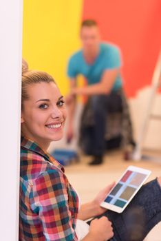 Happy couple doing home renovations, the man is painting the room and the woman is relaxing on the floor and connecting with a tablet