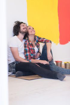 Happy young couple relaxing after painting a room in their new house on the floor