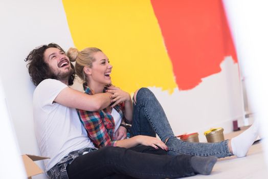 Happy young couple relaxing after painting a room in their new house on the floor