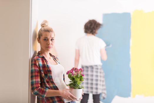 Happy couple doing home renovations, the man is painting the room and the woman hold the pot with flowers