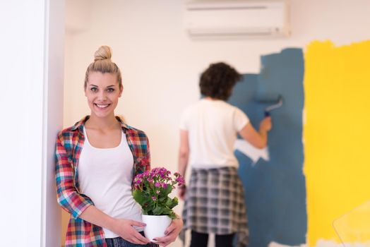 Happy couple doing home renovations, the man is painting the room and the woman hold the pot with flowers