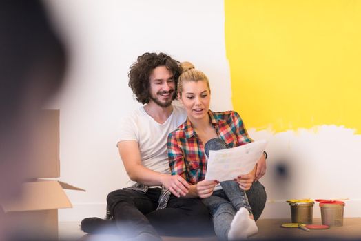 Happy young couple relaxing after painting a room in their new house on the floor