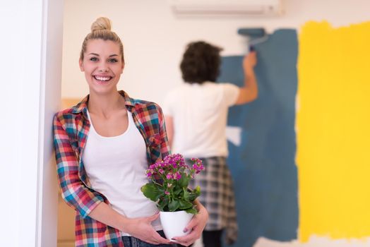 Happy couple doing home renovations, the man is painting the room and the woman hold the pot with flowers