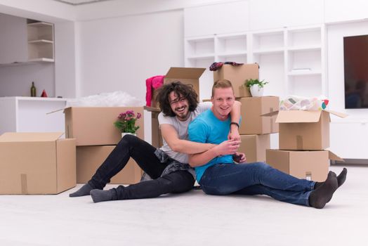 Relaxing in new house. Cheerful young gay couple sitting on the floor while cardboard boxes laying all around them