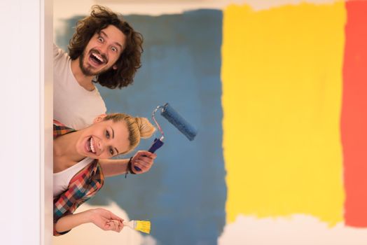 portrait of happy smiling young couple painting interior wall of new house  peeking from behind the wall