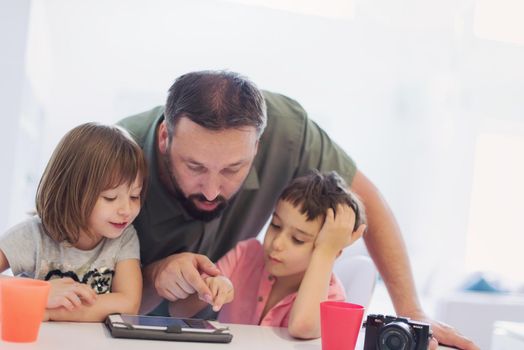 single father at home with two kids playing games and giving education lessons on tablet  computer at modern home