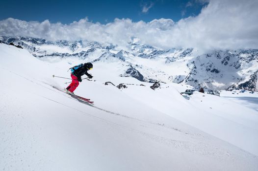 Woman Skier skiing downhill in high mountains against mountains and clouds