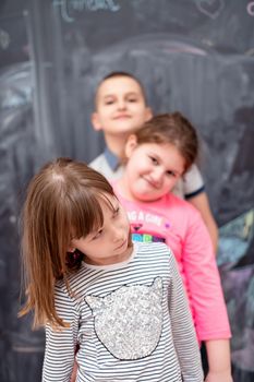 group portrait of happy childrens standing one behind the other while having fun in front of black chalkboard