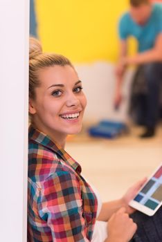 Happy couple doing home renovations, the man is painting the room and the woman is relaxing on the floor and connecting with a tablet