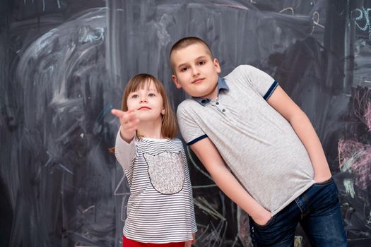 group portrait of happy childrens boy and little girl standing in front of black chalkboard