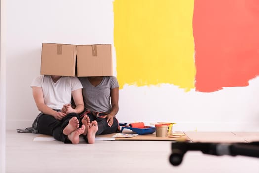 Happy young multiethnic couple relaxing and playing with cardboard boxes after painting a room in their new house on the floor