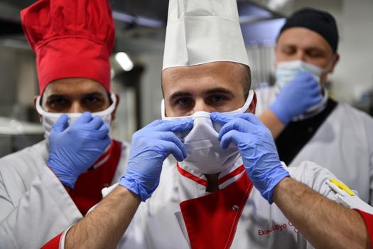 Mixed race team Portrait of group chefs standing together in the kitchen at restaurant wearing protective medical mask and gloves in coronavirus new normal concept