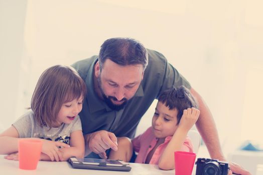 single father at home with two kids playing games and giving education lessons on tablet  computer at modern home
