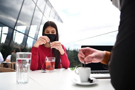 couple with protective medical mask  having coffee break in a restaurant, new normal coronavirus concept