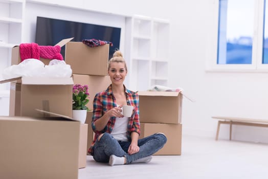 people, moving new place and repair concept   happy beautiful  young woman with many cardboard boxes sitting on floor with Cup at home