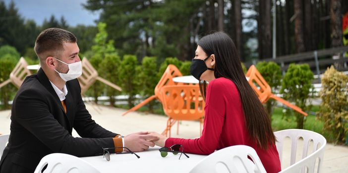 couple with protective medical mask  having coffee break in a restaurant, new normal coronavirus concept