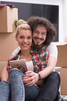 Relaxing in new house. Cheerful young couple sitting on the floor while cardboard boxes laying all around them