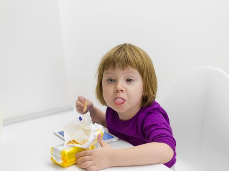 cute little girl eating a cookie while playing games on tablet computer at home