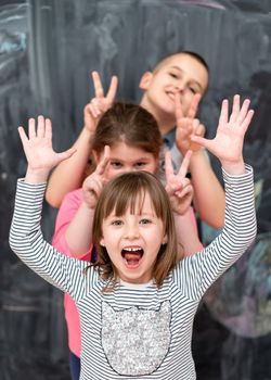 group portrait of happy childrens standing one behind the other while having fun in front of black chalkboard