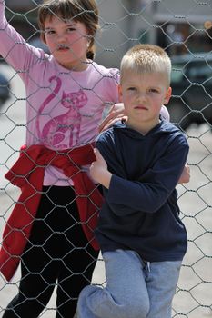 young boy and girl standing over iron fence at day and representing urban and fashion concept for child